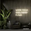 Where Focus Goes Energy Flows neon sign in neutral white for productivity decor and creative inspiration.